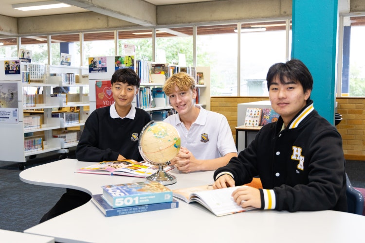 Three students in the library with a globe and books sitting at a desk