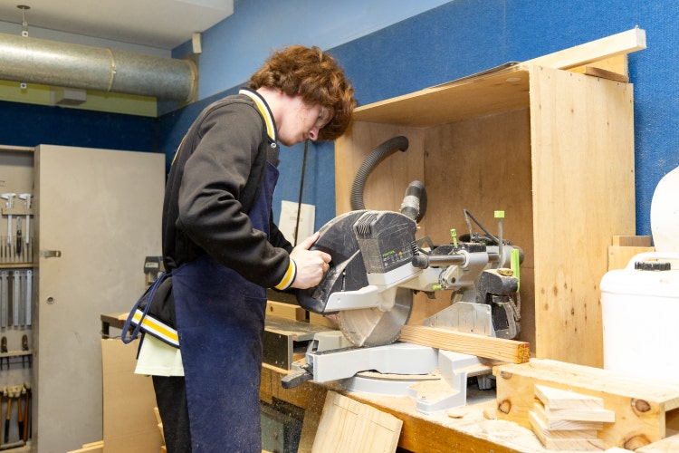 Student learning how to use a saw in Industrial Arts